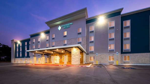 A hotel with a covered entrance, multiple floors, and a sign reading "Woodspring Suites." - WoodSpring Suites Dallas Plano Central Legacy Drive (Plano)