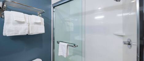 A bathroom with a glass shower enclosure, a white toilet, and a towel rack with two towels.