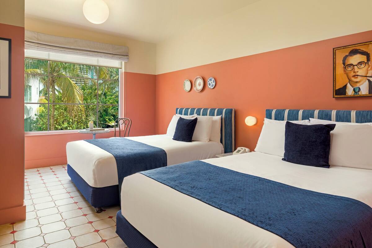 A hotel room with two beds, a window with a view of greenery, a painting on the wall, and a clock.