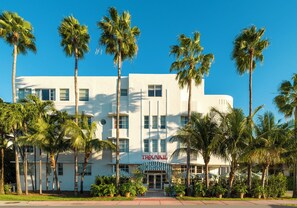 A white building with a sign reading 'TROUVAULT' and 'Resorts.' It has multiple windows and is surrounded by palm trees.