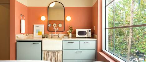 Une salle de bain équipée d’un lavabo, d’un miroir, d’un porte-serviettes et d’une fenêtre donnant sur la verdure.