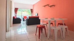 A modern living room with a white tiled floor, a black sofa, a red sofa, and a white dining table with four chairs. - Cameron Highlands (Cameron Jaya) (Cameron Highlands)