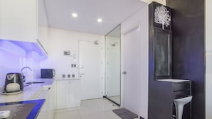 A modern kitchen with a coffee machine, a microwave, and a sink. There is a glass door leading to a bathroom. - Joseph's Place @ Avenir Condo w/ NETFLIX (Cebu City)