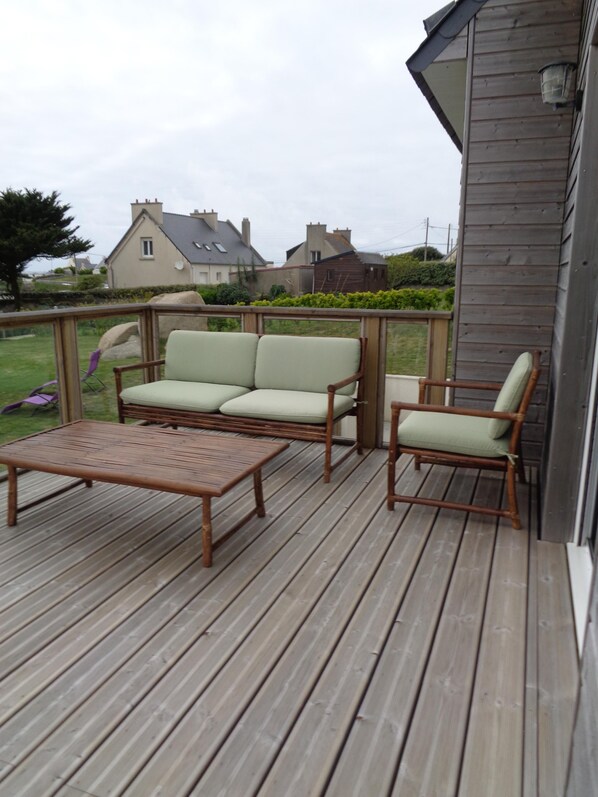 A wooden deck with a sofa and two chairs, a table, and a railing.