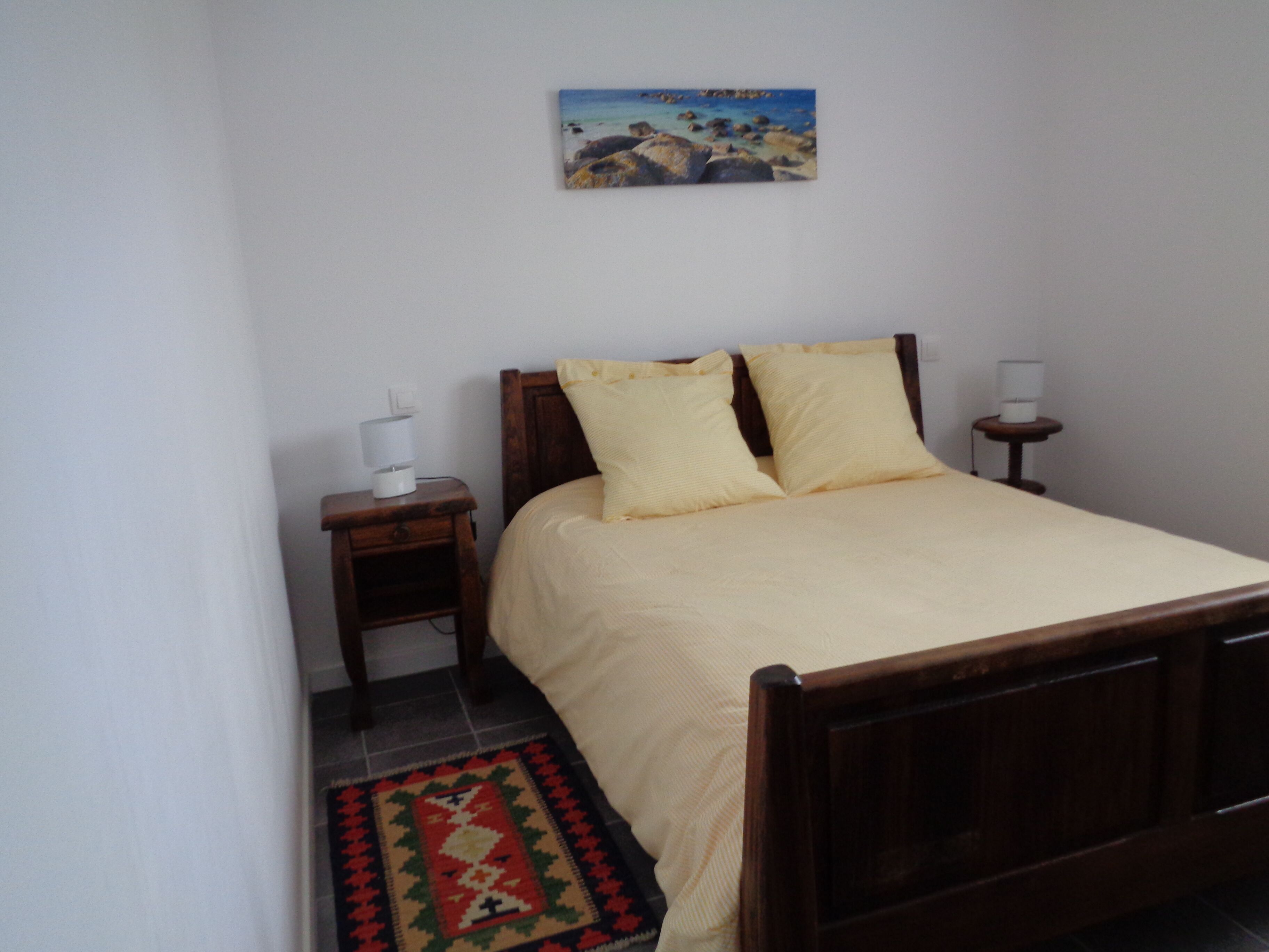 A bedroom with a bed, two bedside tables, a nightstand, a wall-mounted lamp, and a painting.
