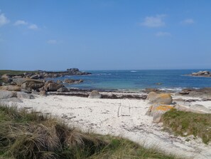A coastal landscape with large rocks, sandy beach, and clear blue sea.