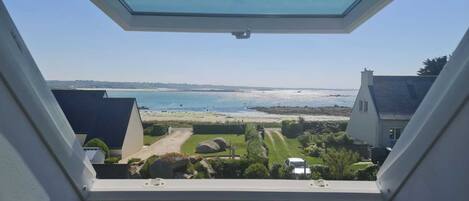 Vista desde una ventana sobre una playa con cielo despejado.