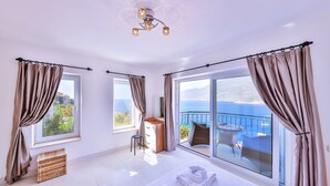 A bedroom with a large bed, a dresser, a chair, and a balcony with a view of the sea. - Villa Mavi Manzara / Luxury, secluded private villa (Kas)