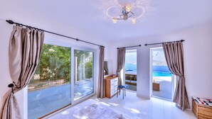 A hotel room with a large sliding glass door to a balcony, a bed with white linens, and a view of the sea. - Villa Mavi Manzara / Luxury, secluded private villa (Kas)