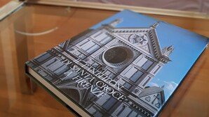 Een boek met de titel 'Il Pantheon a Firenze' op een glazen tafel in een woonkamer, met een bank en een kast op de achtergrond.