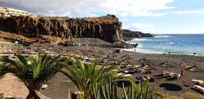 Una playa con acantilados rocosos, sillas de descanso y sombrillas.