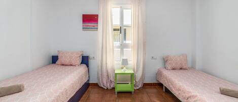 A small, clean room with two beds, a green nightstand, and a window with curtains.