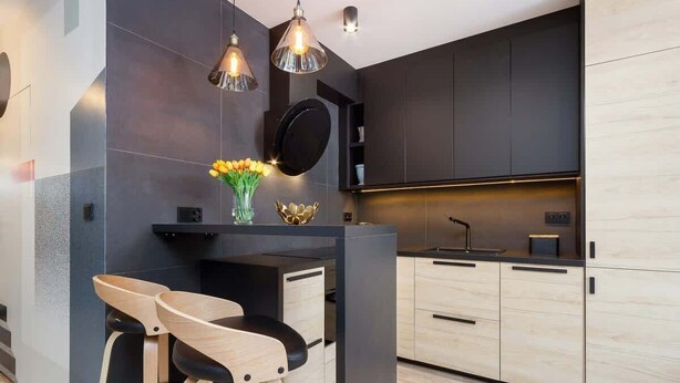 Una cocina moderna con armarios oscuros, una isla central con taburetes, iluminación colgante y un jarrón con flores.