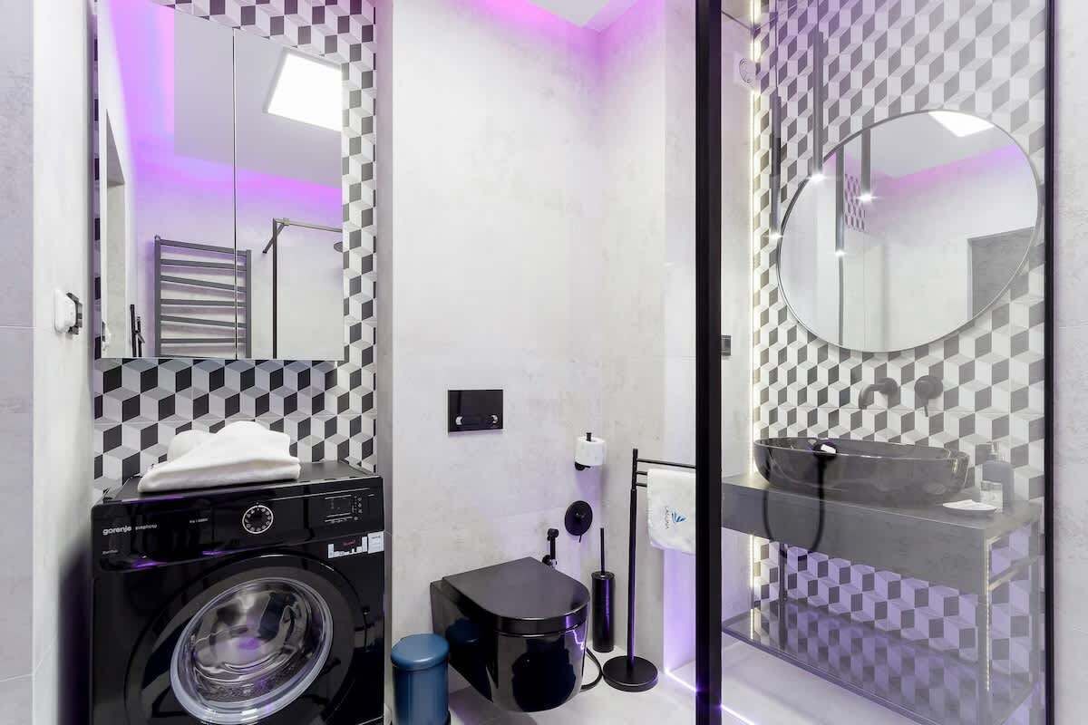 Un baño moderno con una lavadora negra, un lavamanos de vidrio y un patrón de pared a cuadros.
