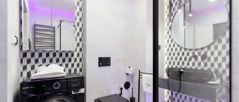 Un baño moderno con una lavadora negra, un lavamanos de vidrio y un patrón de pared a cuadros.