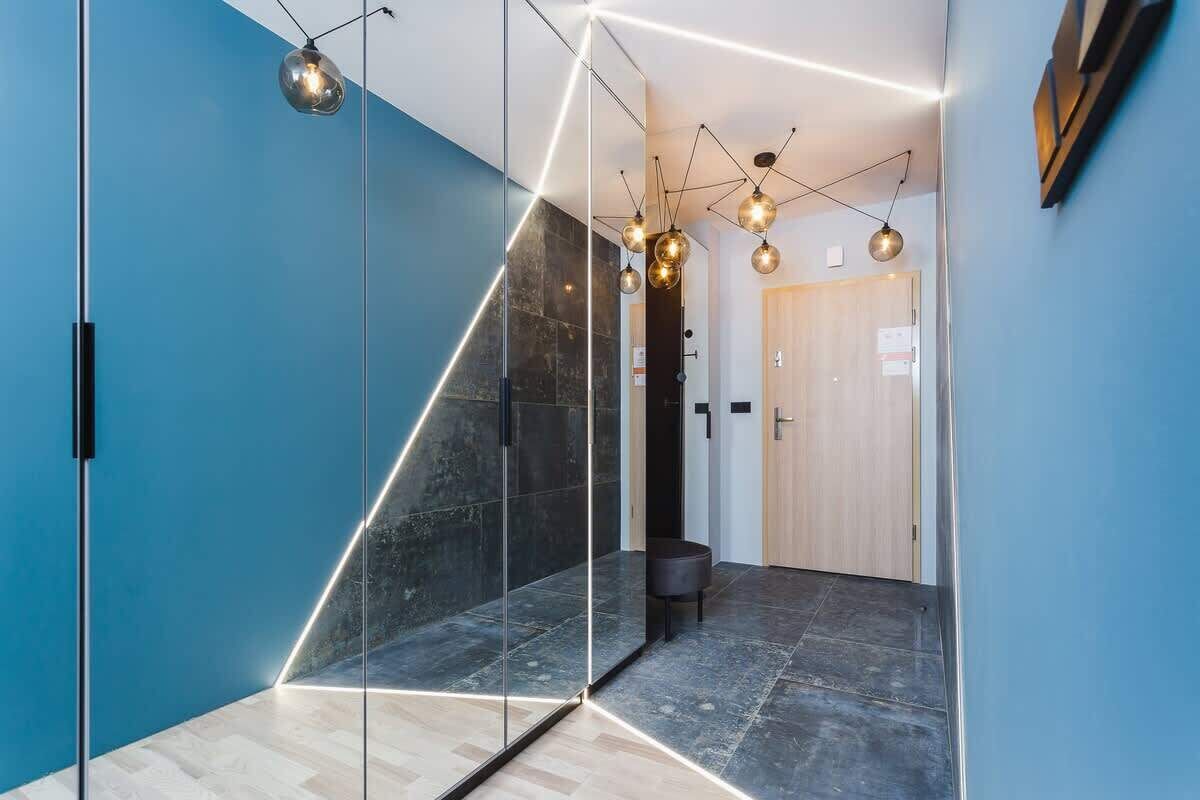 A modern hallway with a geometric glass partition, a wooden door, and contemporary lighting fixtures.