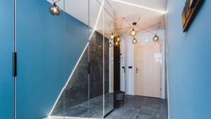 Un pasillo moderno con un separador de vidrio geométrico, una puerta de madera y lámparas contemporáneas.