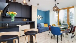 Una cocina moderna con armarios negros, una isla central y taburetes de madera. Hay una zona de comedor con un sofá azul, una mesa redonda y sillas.
