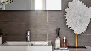 A modern bathroom with a large mirror, a sink, and a toilet. There is a decorative white flower arrangement on the wall.