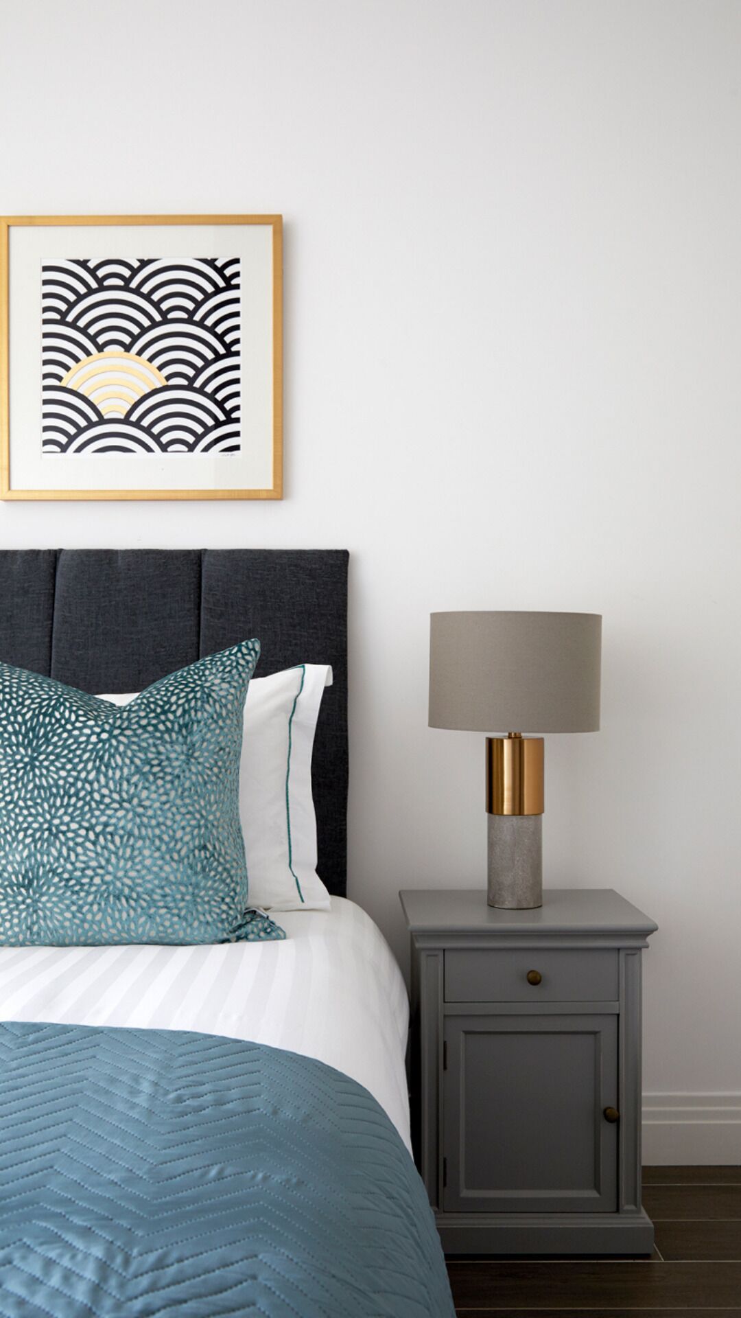 A neatly made bed with a patterned pillow, a bedside table with a lamp, and a framed artwork on the wall.