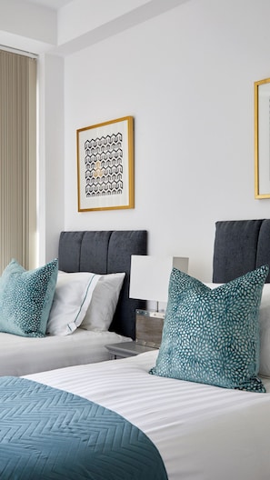 A hotel room with two beds, a grey headboard, and a framed abstract artwork on the wall.
