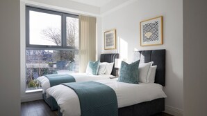 A modern bedroom with two beds, large windows, and artwork on the walls.