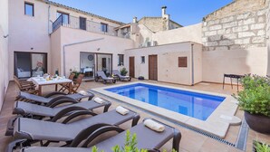 A pool area with lounge chairs and a table, surrounded by buildings with balconies and a stone wall. - Casa Sa Placeta by JS Villas (Sa Pobla)