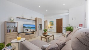 A modern living room with a sofa, a coffee table, a TV, and a bookshelf. - Casa Sa Placeta by JS Villas (Sa Pobla)