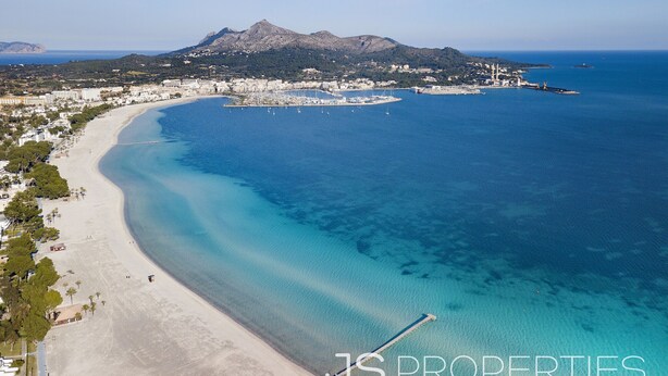 An aerial view of a coastal area with a beach, marina, and mountainous backdrop. - Casa Sa Placeta by JS Villas (Sa Pobla)