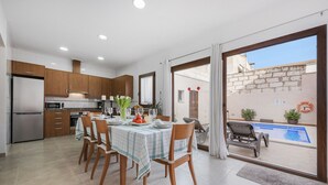 A modern kitchen with wooden cabinets, a dining area with a table set for four, and a view of a swimming pool through large glass doors. - Casa Sa Placeta by JS Villas (Sa Pobla)
