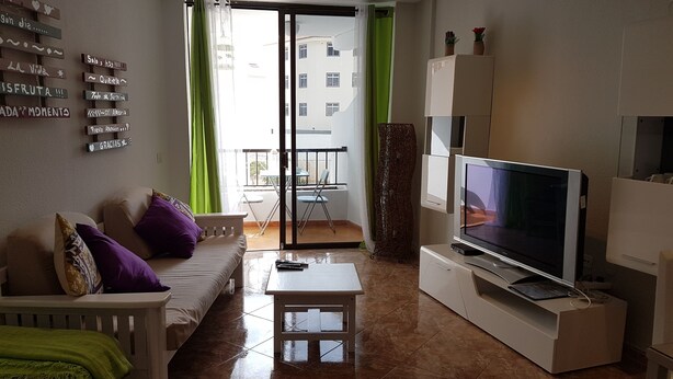 A living room with a sofa, TV, and a balcony with a table and chairs. - Los Cristianos Apartment Nirvana Tenerife South (Los Cristianos)