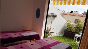A room with two beds, a small table, and a view of a garden. - Los Cristianos Apartment Nirvana Tenerife South (Los Cristianos)