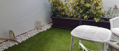 A small balcony with artificial grass, white wicker furniture, and potted plants.