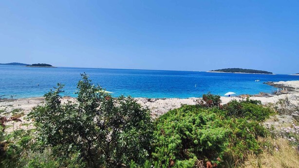 Paisaje costero con mar azul cristalino, costa rocosa e islas a lo lejos.