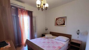 Un dormitorio con cama, mesita de noche, lámpara de pared, un cuadro y una ventana con cortinas.