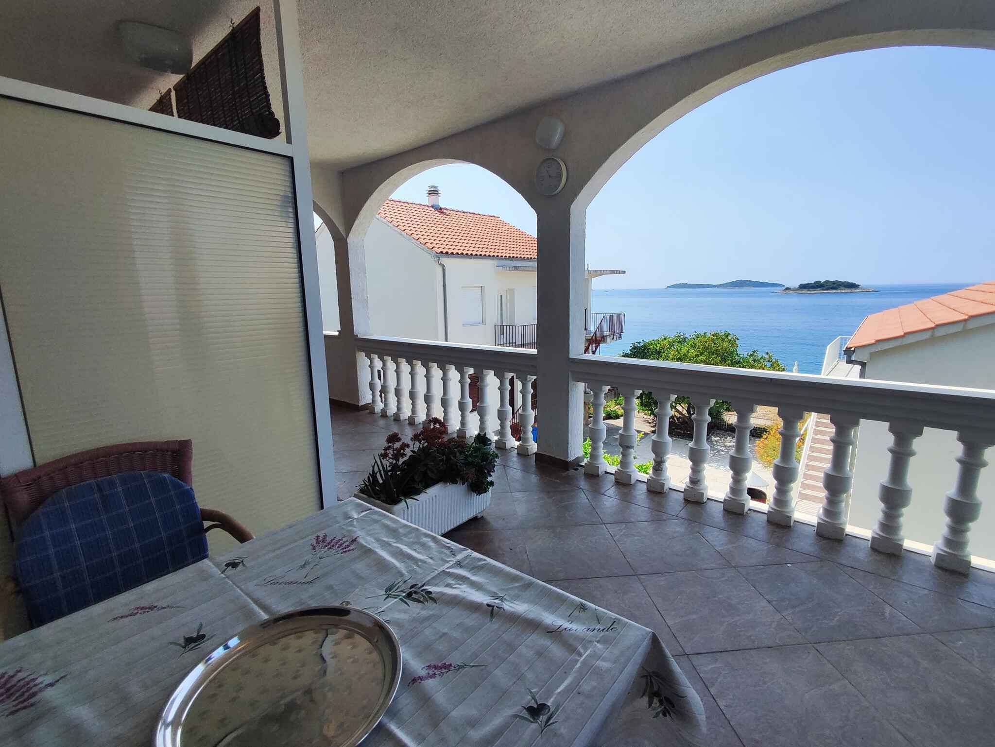 A balcony with a view of the sea, a table with a metal tray, and a chair with a blue cushion.