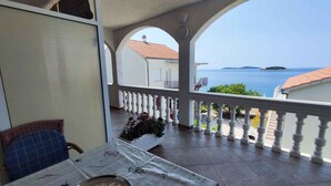 Un balcón con vistas al mar, una mesa con una bandeja metálica y una silla con cojín azul.