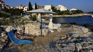 A rocky beach with lounge chairs and umbrellas, overlooking a calm sea and coastal buildings.