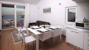 A modern living room with a dining area, a kitchen, and a balcony with a view of the sea.