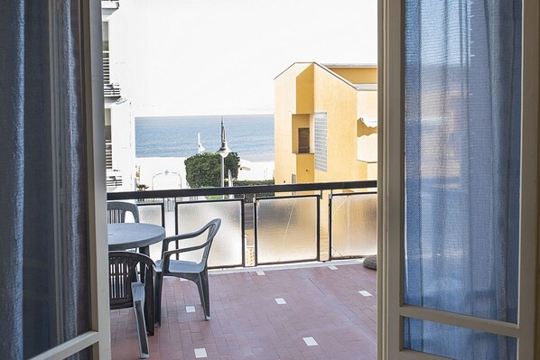 A balcony with a table and chairs, a view of the sea, and a building with a yellow facade.