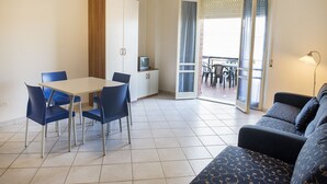 Ein Zimmer mit Esstisch, Stühlen, einer Couch, einem Fernseher und einer Schiebetür zu einem Außenbereich.