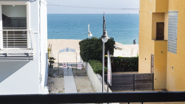 Blick auf die Küste mit blauem Himmel, Sandstrand und einem Gebäude mit Balkon.