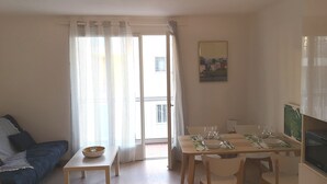 A living room with a sofa, a dining table set for four, and a kitchen area with a microwave and refrigerator.