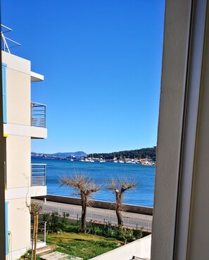 Uitzicht vanaf een balkon op een jachthaven met boten, een heldere blauwe lucht en een heuvelachtig landschap in de verte.