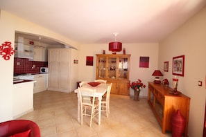 Cozinha compacta com área de refeições, um armário com portas de vidro e um vaso vermelho na mesa.