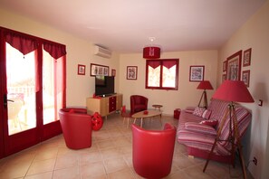 Uma sala de estar com sofá, cadeiras vermelhas, televisão e um espaço de jantar com mesa e cadeiras.