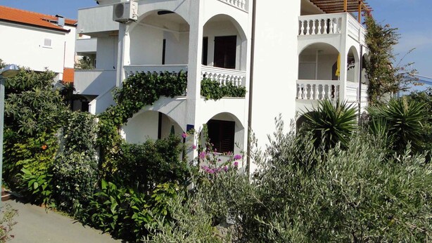 Ein zweistöckiges Gebäude mit Balkonen, Bogenfenstern und einem Garten davor.