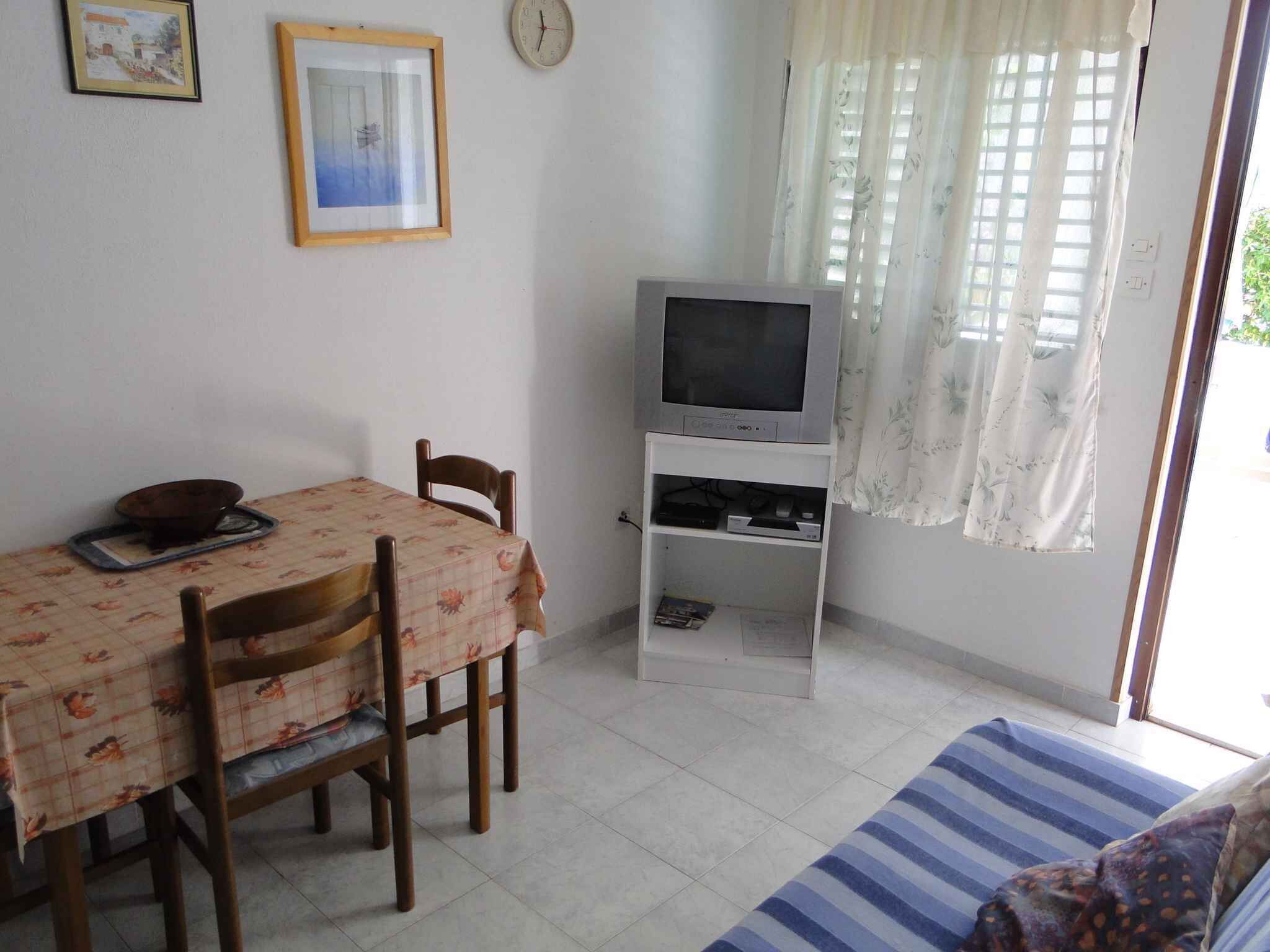 A small room with a dining table, chairs, a television on a stand, and a window with curtains.
