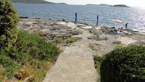 Ein felsiger Strand mit einem klaren Weg zum Wasser, einigen Sonnenschirmen und einem weiten Blick auf das Meer.