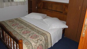 Ein Schlafzimmer mit einem Holzkopfende, einer blumigen Bettdecke und einem Nachttisch mit einer Lampe.